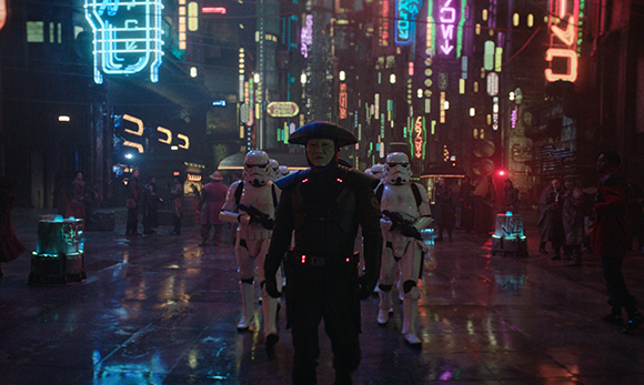 Stormtroopers and a dark-clad officer walk down a wet, neon-lit futuristic city street at night.