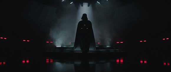Silhouette of a cloaked figure standing on a platform amidst smoke and red lights.