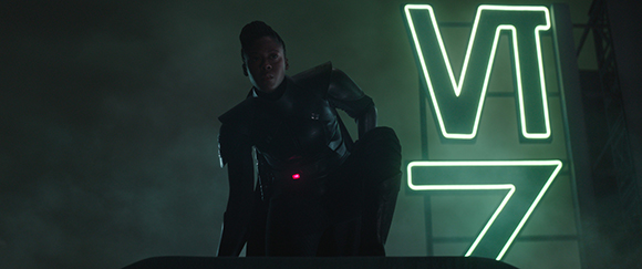 A person in dark tactical armor crouches before a large, glowing green VT7 neon sign in a dark, smoky room.
