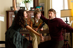 A woman, a boy, and a man make exaggerated surprised expressions with mouths open in a living room.