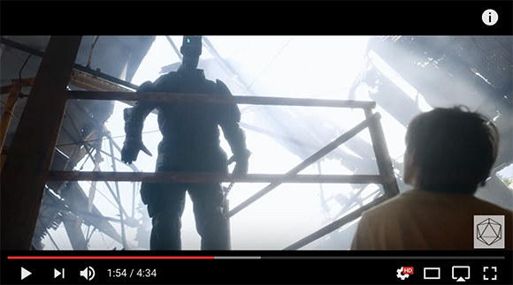 Silhouette of a large humanoid robot standing behind metal scaffolding in bright light.