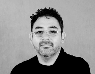 Black and white headshot of a man with dark hair, glasses, and a short beard looking forward.