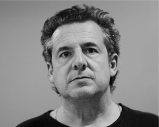 Black and white close-up portrait of a man with wavy hair looking directly forward.