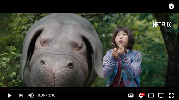 A young girl in a colorful jacket stands next to a large hippopotamus in a lush green forest.