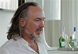 A man with long greyish hair and a goatee wearing a white shirt.