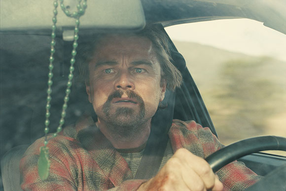 A man with a mustache and light brown hair looks forward while driving a vehicle.