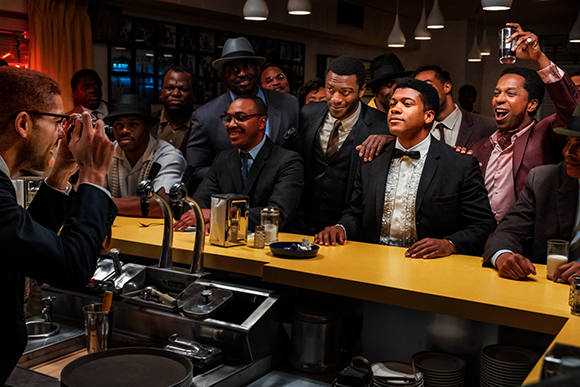 A group of men in suits and formal attire smiling and posing behind a bar counter.