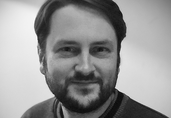Black and white close-up portrait of a man with dark hair and a beard looking toward the camera.
