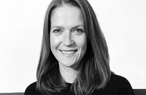 A smiling woman with long hair looks directly at the camera in a black and white portrait.