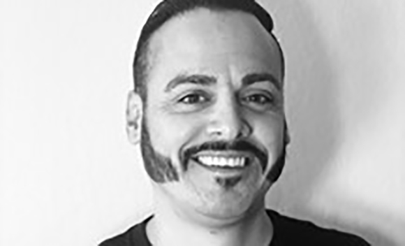 Black and white portrait of a smiling man with a dark beard and mustache.