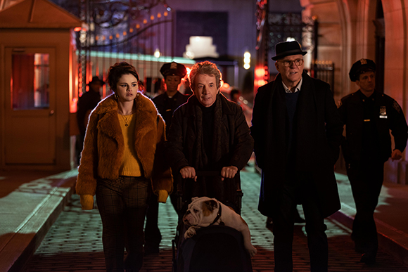 A woman in a yellow sweater and fur coat walks alongside an older man in a black coat and a man in a wheelchair.