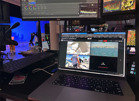 A laptop and two large monitors displaying video editing software and various video clips in a studio setting.