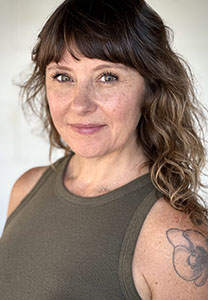 A woman with wavy brown hair and bangs smiles slightly at the camera.