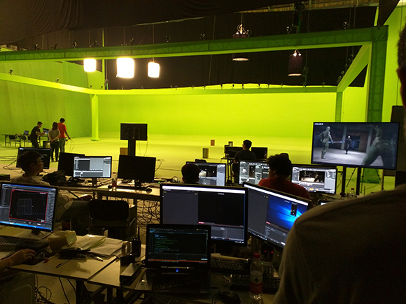 Crew members working with multiple computer monitors in a large green screen studio.