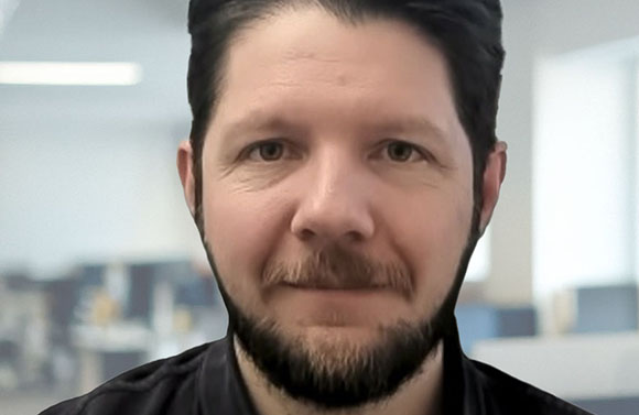Close-up portrait of a man with dark hair and a beard looking directly at the camera.
