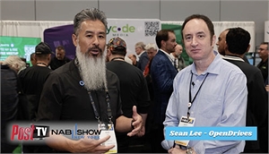 A man with a long grey beard and a man in a light blue shirt stand at a convention.