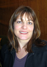 A smiling woman with shoulder-length brown hair and bangs wearing a dark jacket.