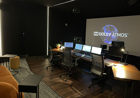 A dark sound mixing studio with a large screen displaying the Dolby Atmos logo and multiple computer monitors.