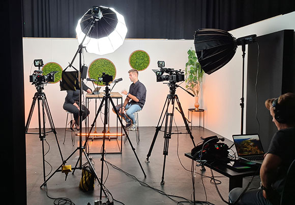 A film studio setup with cameras on tripods, studio lights, and two people seated for an interview.