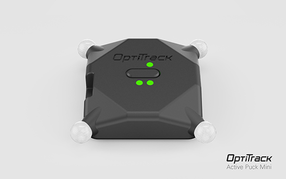 A black square OptiTrack Active Puck Mini with four white spherical markers at the corners.