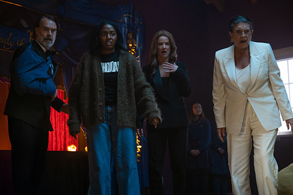 Five people with worried or shocked expressions stand together in a dark room.