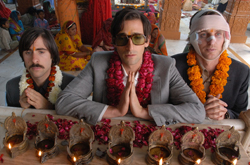 Three men in suits and garlands sit behind a table decorated with rose petals and small oil lamps.