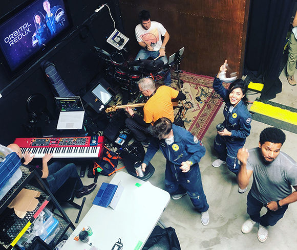 High-angle view of musicians with a drum kit, keyboard, and guitar in a studio setting.