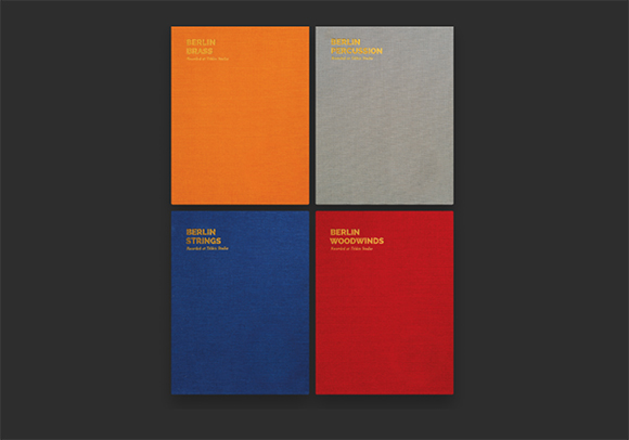 Four textured book covers in orange, grey, blue, and red arranged in a two-by-two grid on a dark background.