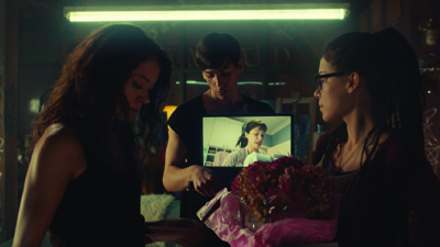 Three young women gather closely to look at a small photograph held between them.