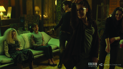 Several people gather in a dark, moody room with warm lighting and a green-toned atmosphere.