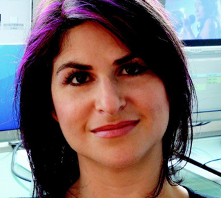 A woman with dark hair featuring purple highlights looks toward the camera.