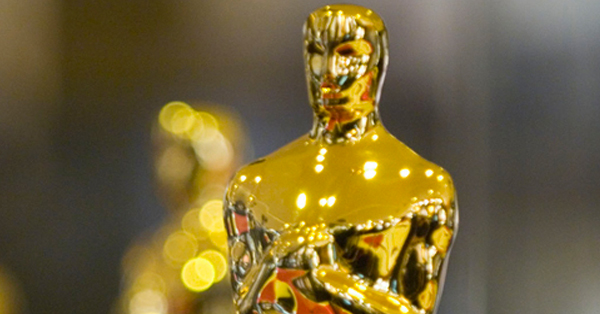 A shiny gold Oscar award statuette in sharp focus against a blurred background.