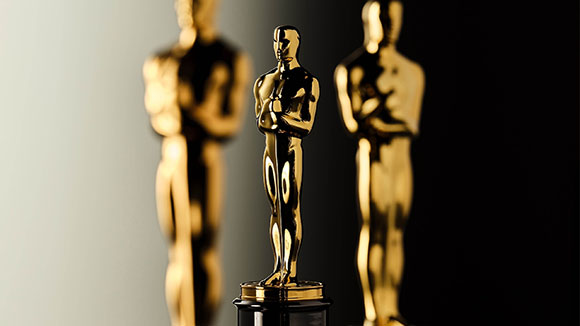 Three gold Academy Award statuettes, with one in sharp focus in the center and two blurred in the background.