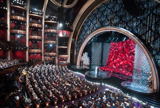 An expansive view of a crowded theater with a large stage featuring a massive red floral arrangement.
