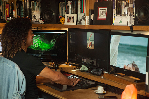 A person sits at a desk using a keyboard and three monitors displaying various digital content.