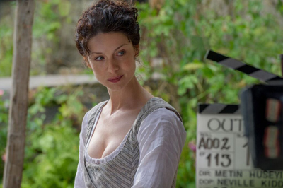 A woman with dark curly hair wearing a white and striped bodice looks sideways near a film clapperboard.