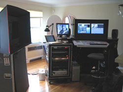 A media editing suite featuring two computer monitors, a large studio monitor speaker, and an equipment rack.