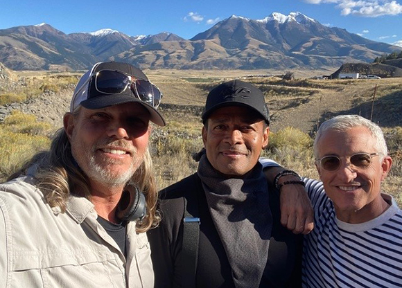 Three men posing for a photo with mountains and a valley in the background.