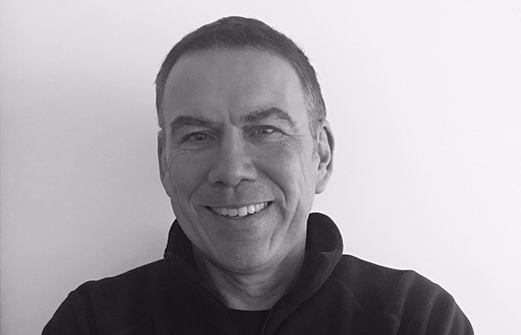 A smiling middle-aged man with short hair looking directly at the camera against a plain background.