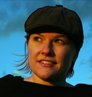 A woman in a dark cap looking upward against a blue sky.