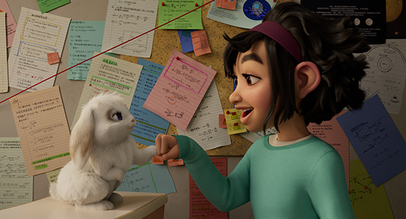 A young girl in a teal shirt smiles at a small white rabbit sitting on a desk in front of a bulletin board.