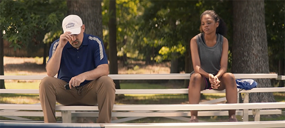 A man in a white cap and blue shirt sits dejectedly on a bench while a young woman sits nearby looking away.