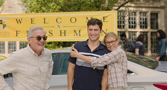 A man and woman hug a younger man in front of a yellow banner that says Welcome Freshmen.
