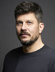 A man with short dark hair, blue eyes, and a salt-and-pepper beard looking toward the camera.