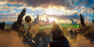 A hot air balloon drifts over a surreal landscape of sharp rock spires and lush green valleys under a sunset sky.