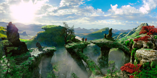 A wide landscape of green mountains, stone arches, and mist under a bright, cloudy sky.