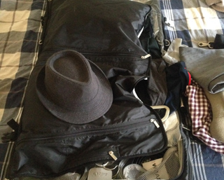 A black fedora hat is placed on an open black garment bag with clothes inside.