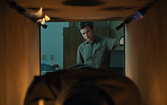 A man peers through a dark, narrow gap toward the camera.
