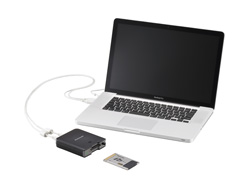 A silver laptop connected by a white cable to a small black external hard drive on a white surface.