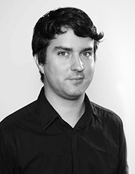 Black and white portrait of a man with dark hair wearing a dark button-down shirt.